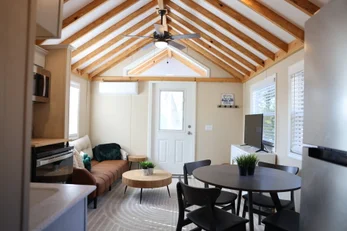 Modern open living room with gray sectional sofa, ceiling fan, wood flooring, and large window - professional Airbnb listing photography