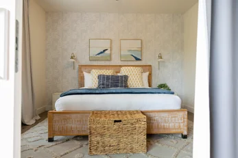 Cozy bedroom with wooden bed frame, white bedding, blue accents, patterned pillows, and rug - professional Airbnb listing photography